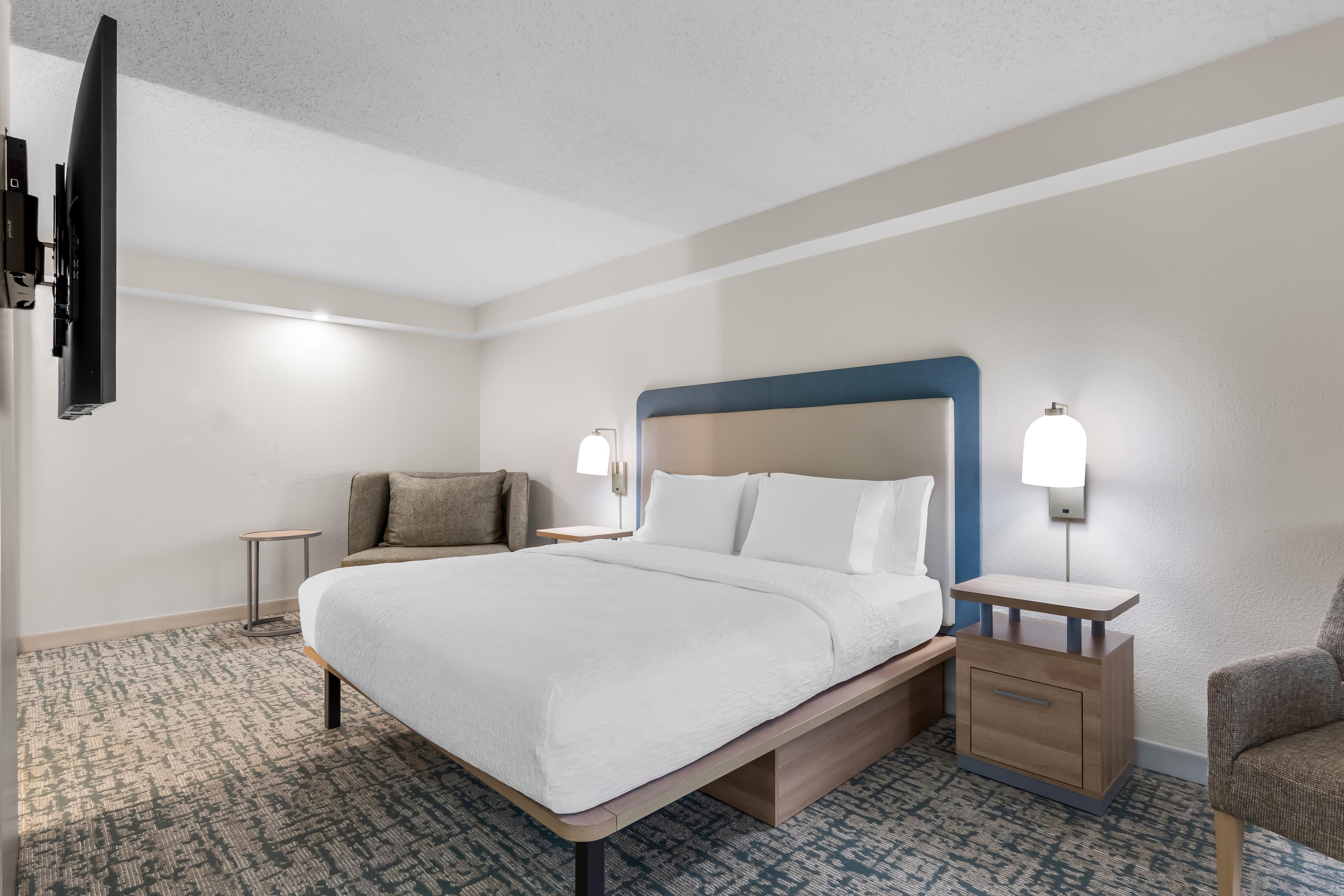 A hotel room with a bed, a chair, a desk, and a TV.