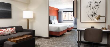 A hotel room with a sofa, a desk, a chair, two beds, and artwork on the walls.