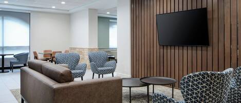 A modern lounge area with a sofa, patterned armchairs, a flat-screen TV, and a wooden panel wall.