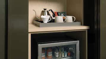 En minibar med en kaffebryggare, koppar och ett litet kylskåp fyllt med drycker.
