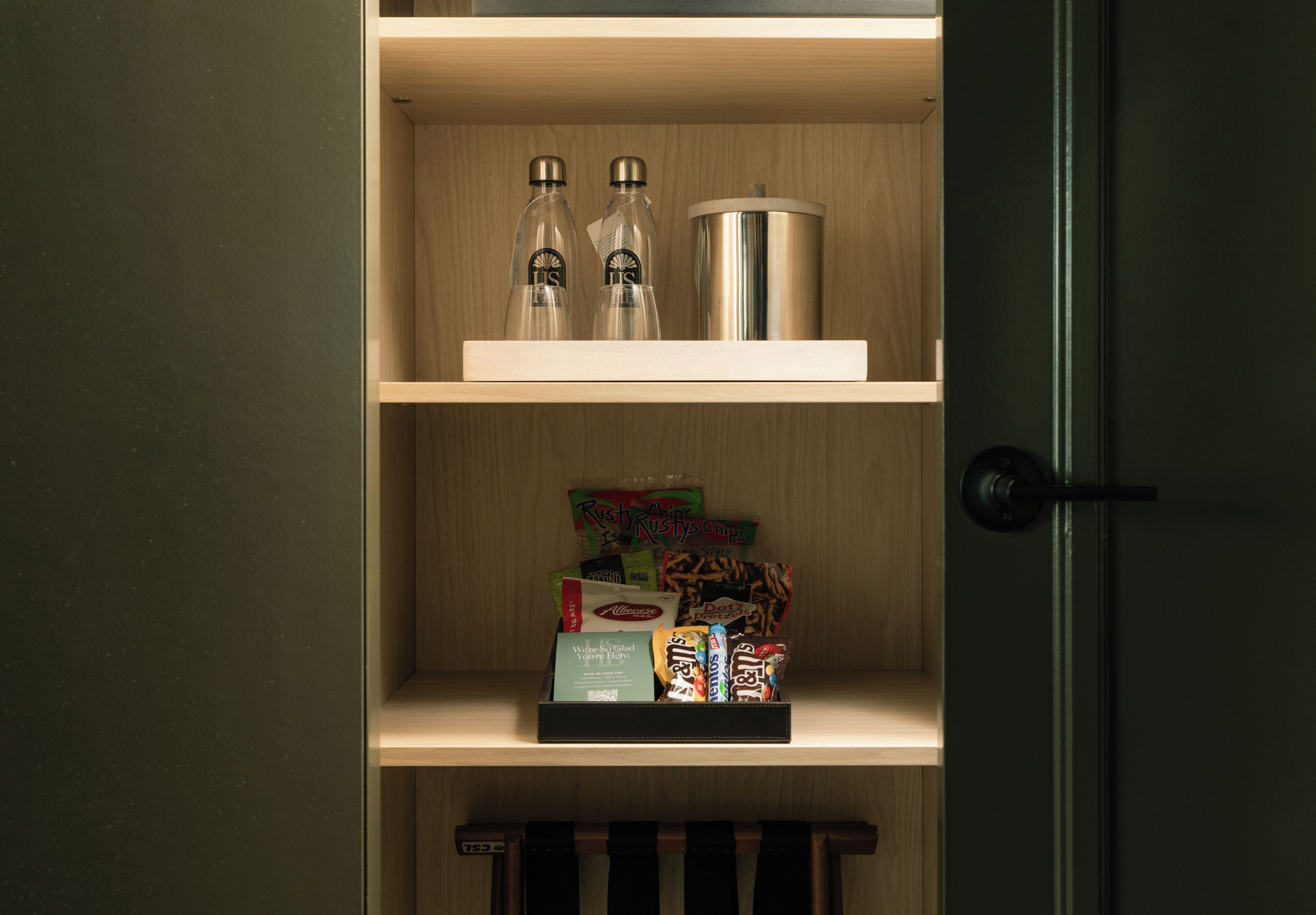 A wooden shelf with two bottles, a metallic container, and a box of snacks.