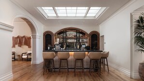 A bar area with a high ceiling and skylight, wooden flooring, and a bar counter with stools.