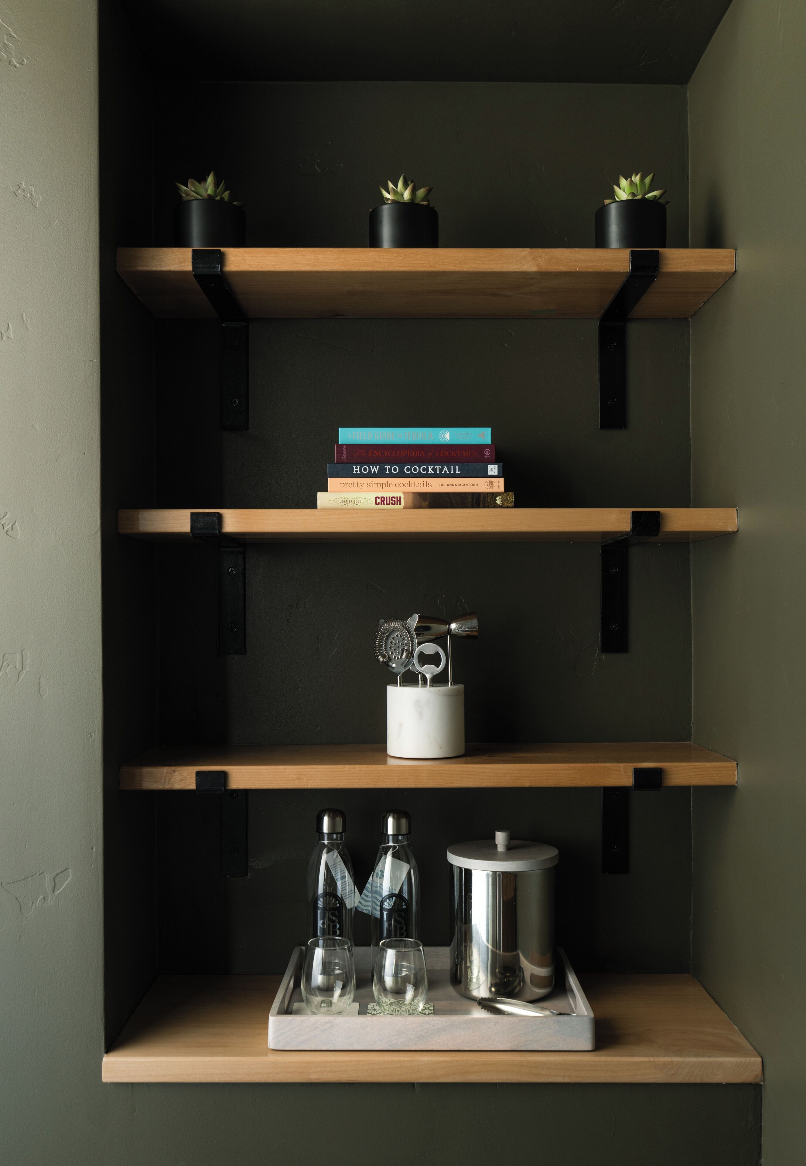 A shelf with books, a cocktail shaker, and glasses.