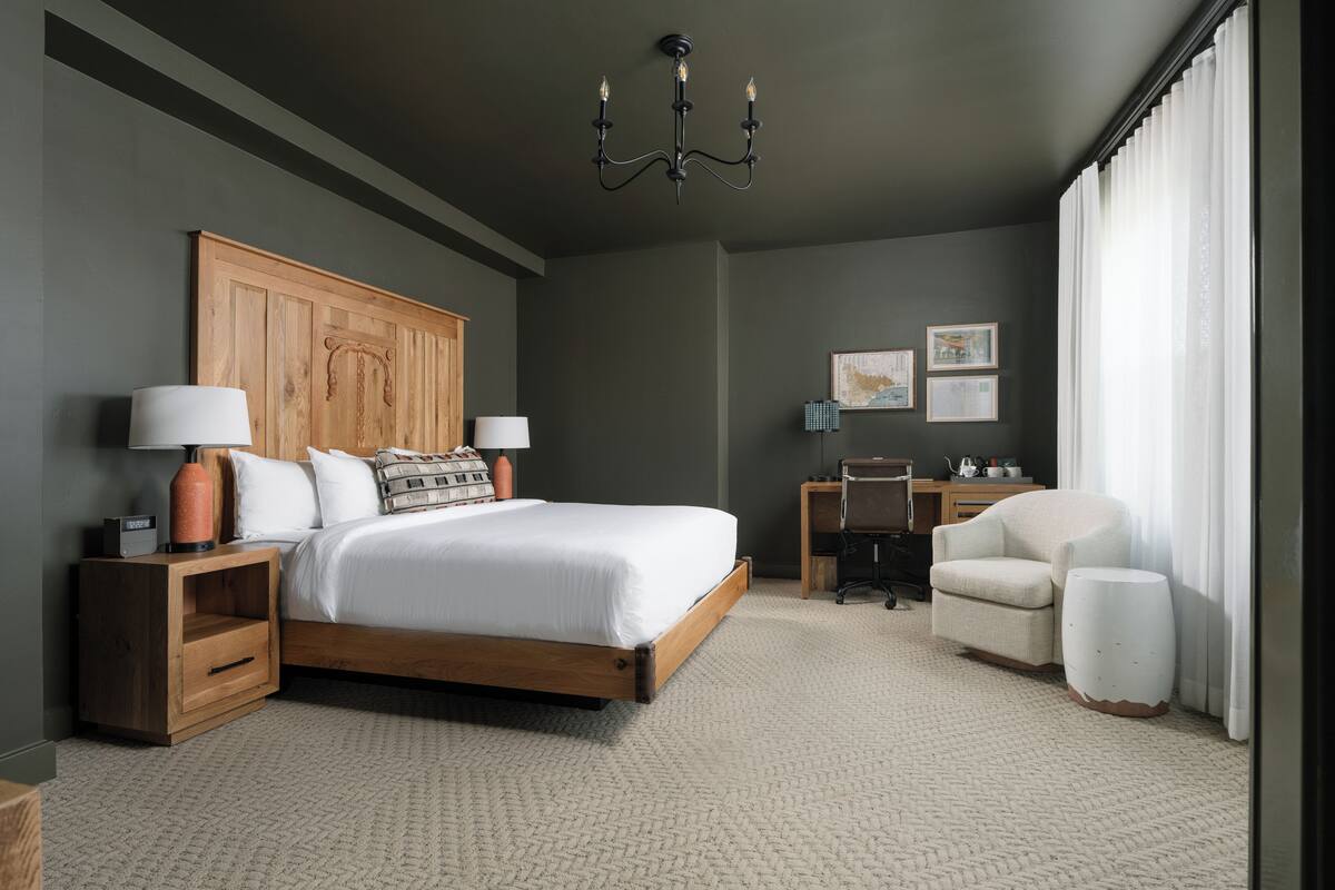 A modern bedroom with a wooden headboard, a large bed, a desk, a chair, and a chandelier.