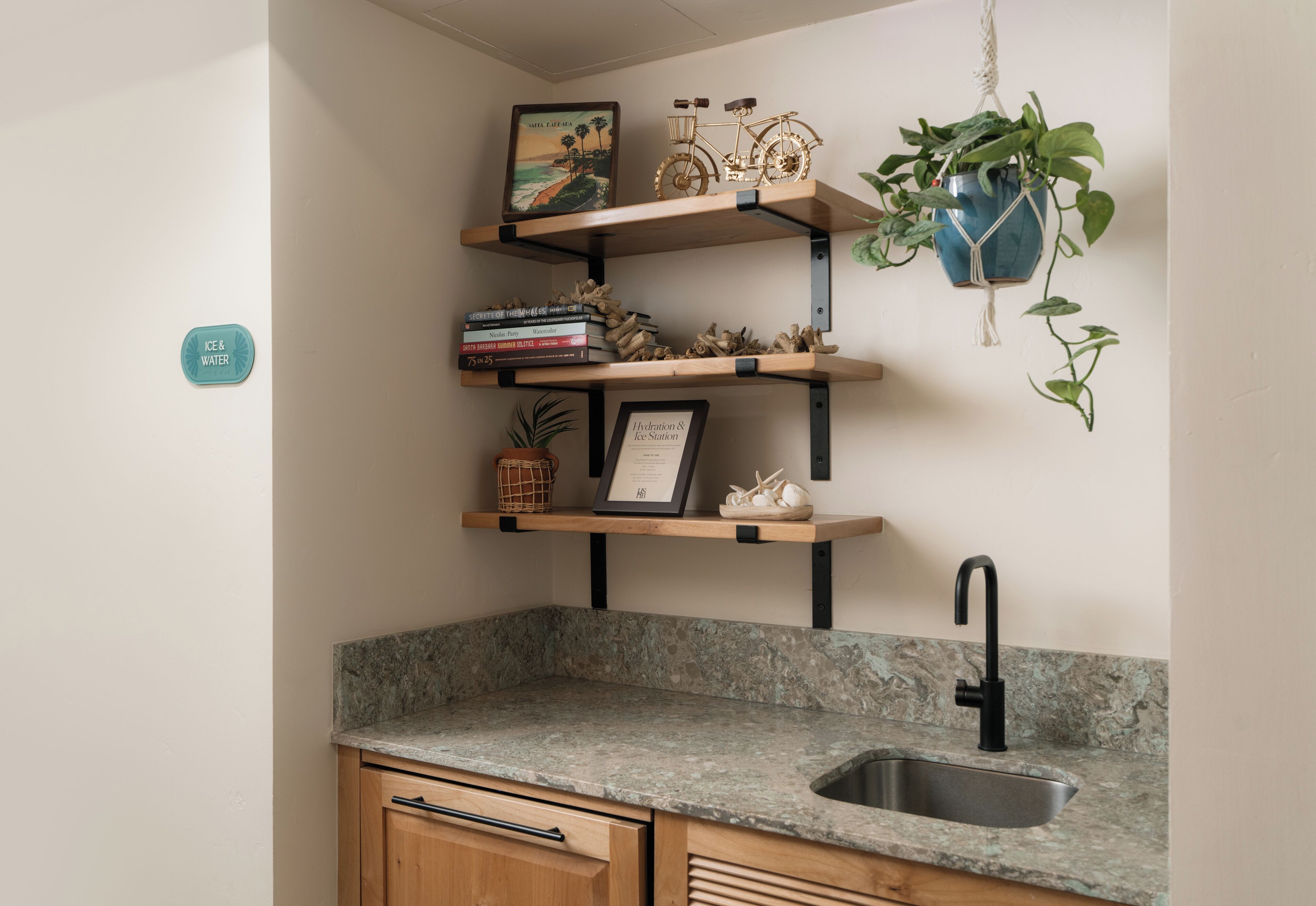 A kitchen with a granite countertop, a black sink, wooden cabinets, and a wall-mounted shelf with books and decorative items.