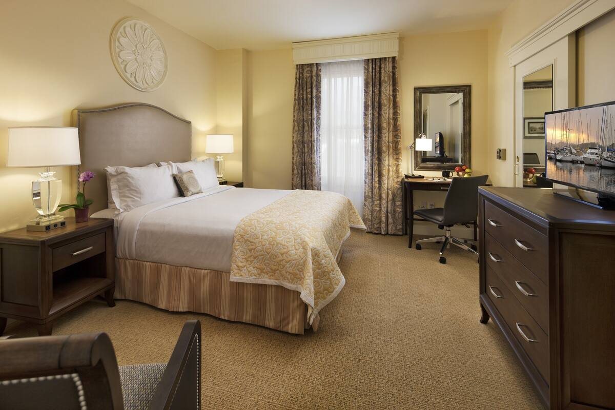 A hotel room with a bed, desk, chair, dresser, and a television.