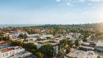An aerial view of a coastal town with white buildings, green trees, and a clear sky.
