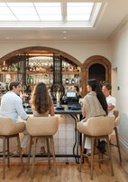 A bar area with a high ceiling and skylight, wooden bar stools, and a well-stocked liquor shelf.