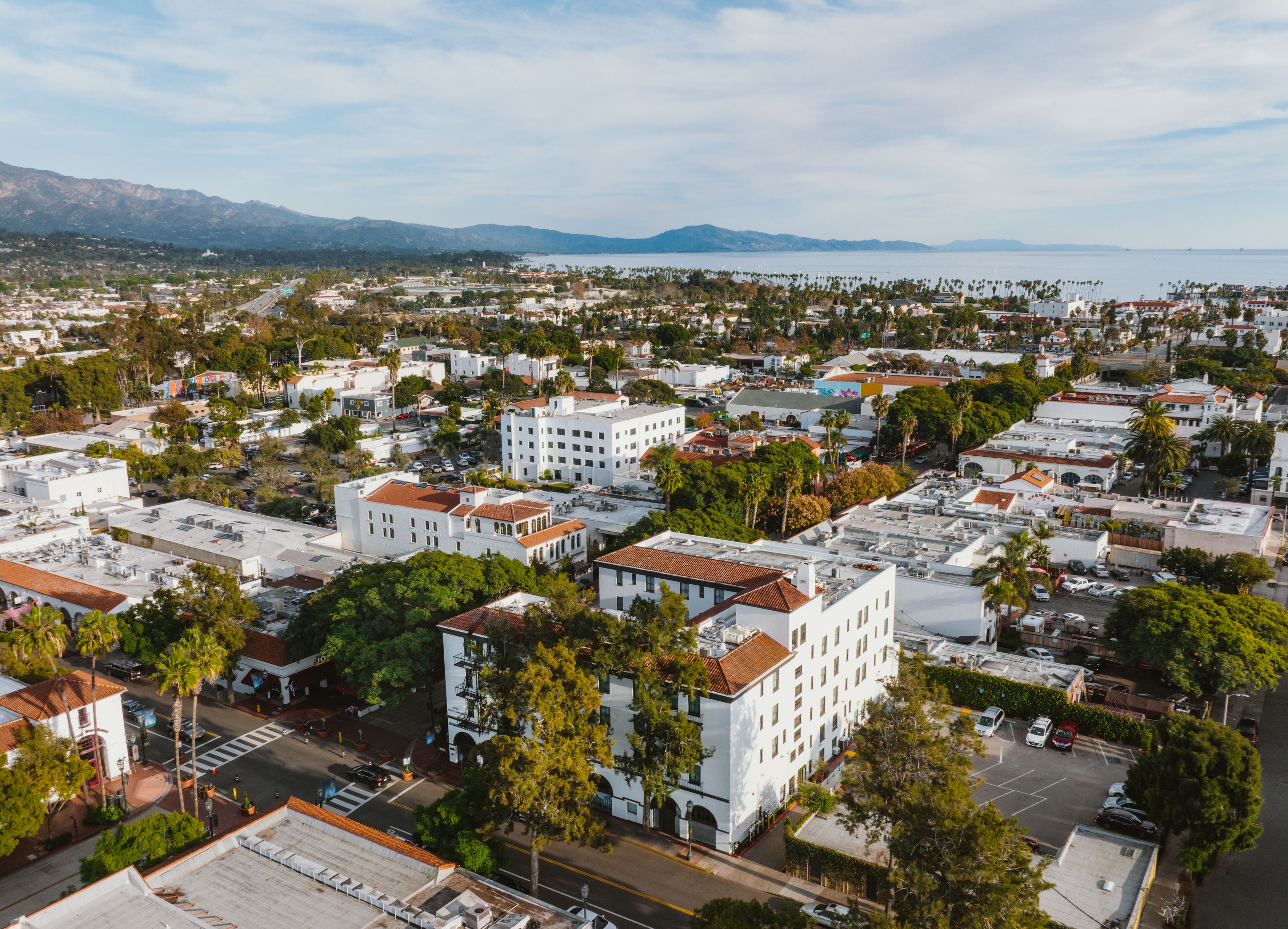 An aerial view of a coastal city with white buildings, green spaces, and a clear view of the ocean.