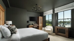 A modern bedroom with a large bed, a desk, a chair, a TV, and a view of the outdoors.