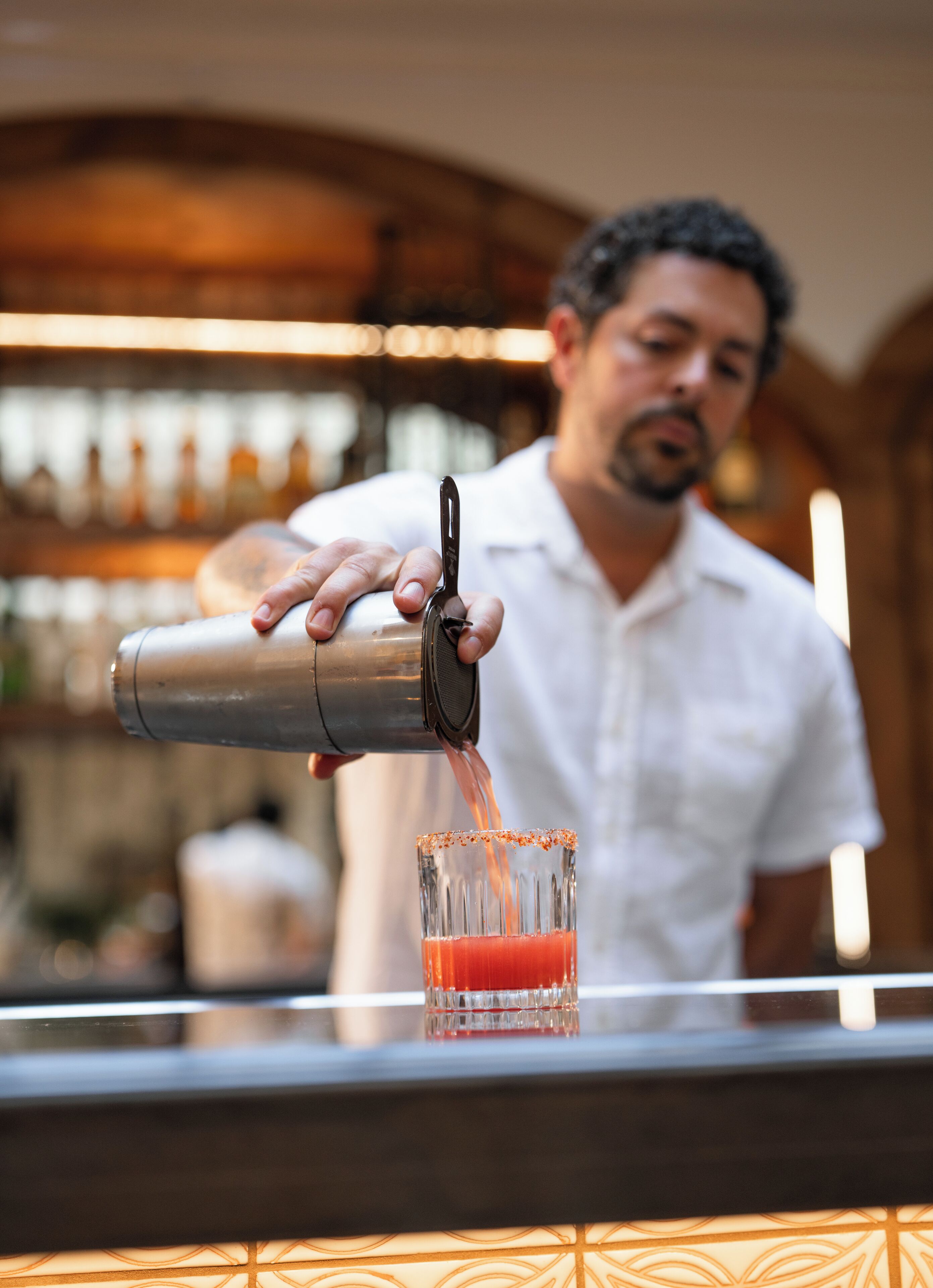 A bartender pouring a drink into a glass.
