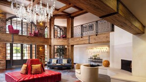 A spacious loft with exposed wooden beams, a red sofa, a white armchair, and a fireplace. - Corque Hotel, Solvang, A Tribute Portfolio Hotel (Solvang)