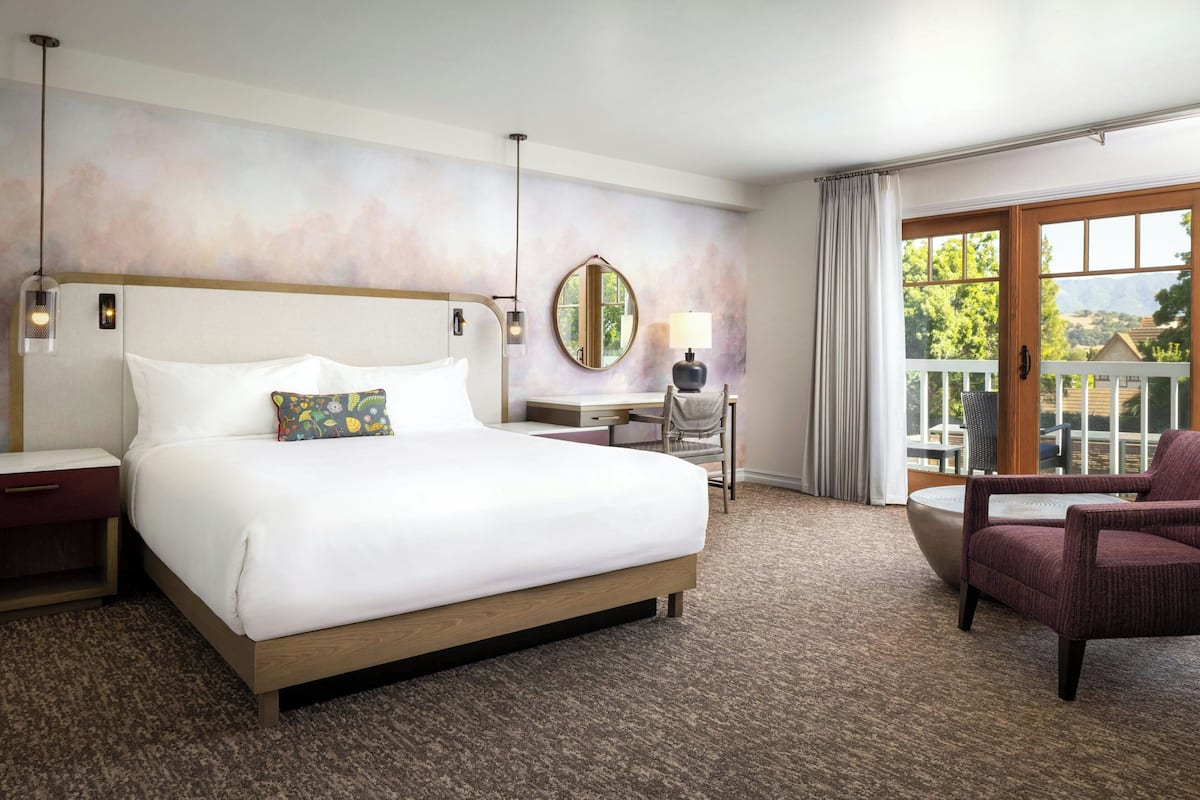 A hotel room with a large bed, a desk, a chair, and a view of the outdoors.