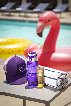 A poolside table with a purple cap, a purple bottle, a golden bottle, and a rolled towel.