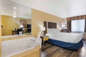 Habitación de hotel con una cama grande, un baño con bañera, un escritorio y una televisión.