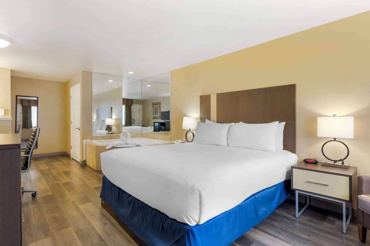Une chambre d’hôtel avec un grand lit, des tables de chevet, un bureau, une chaise et un miroir.