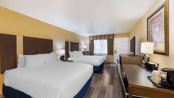 A hotel room with two beds, a desk with a coffee maker, a TV, and a framed picture on the wall.