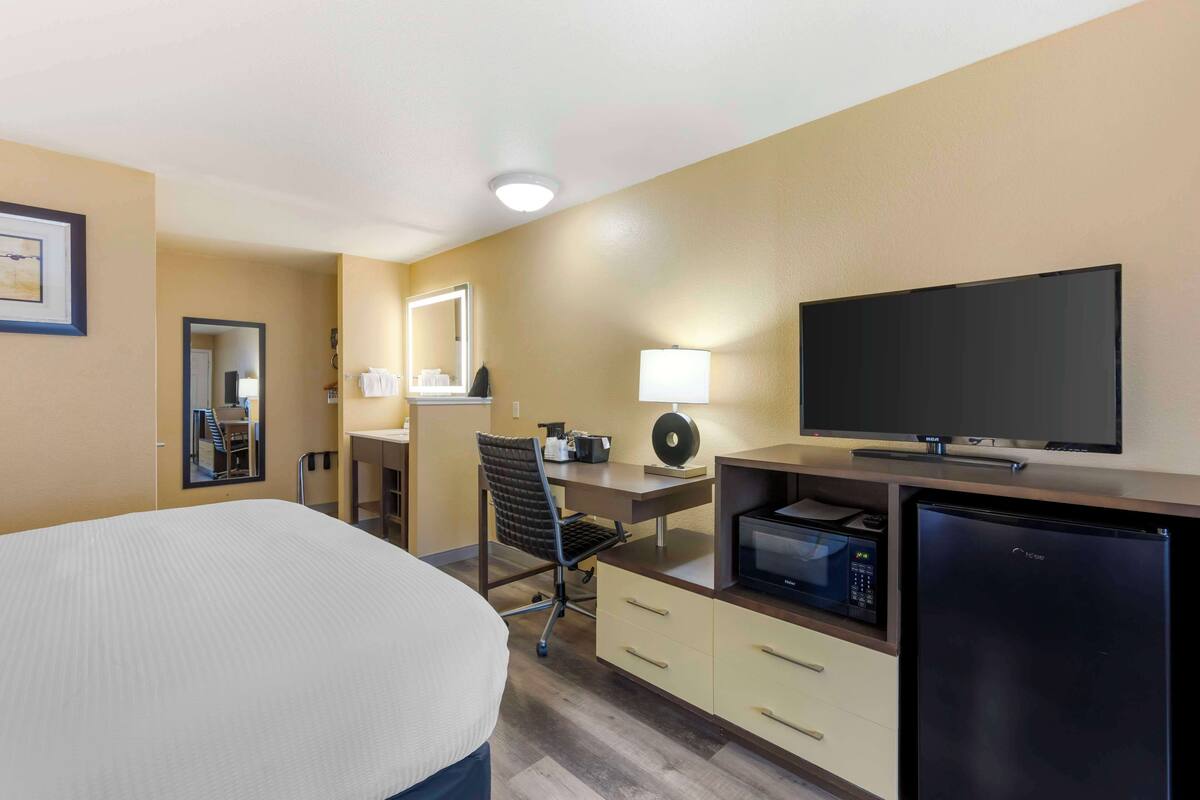 Une chambre d’hôtel équipée d’un lit, d’un bureau, d’une chaise, d’une télévision, d’un four à micro-ondes et d’un réfrigérateur.