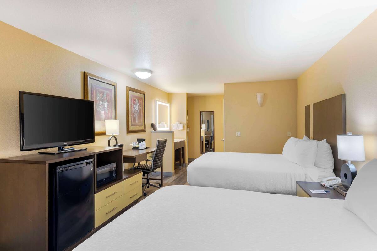 Une chambre d’hôtel avec deux lits, un bureau avec un ordinateur, une télévision, un four à micro-ondes et un réfrigérateur.