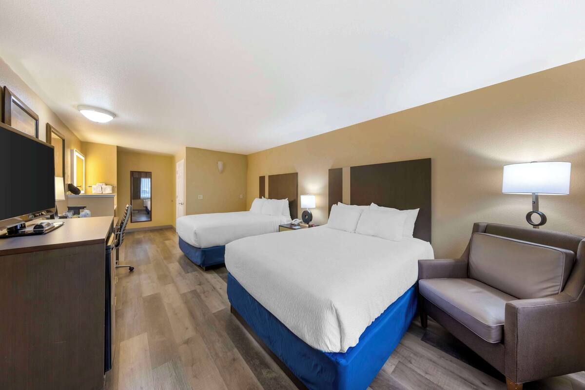 Une chambre d’hôtel avec deux lits, un bureau, une chaise et un téléviseur.