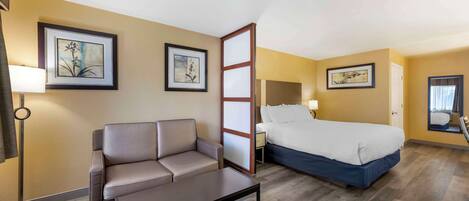 A hotel room with a bed, a sofa, a coffee table, and framed artwork on the walls.
