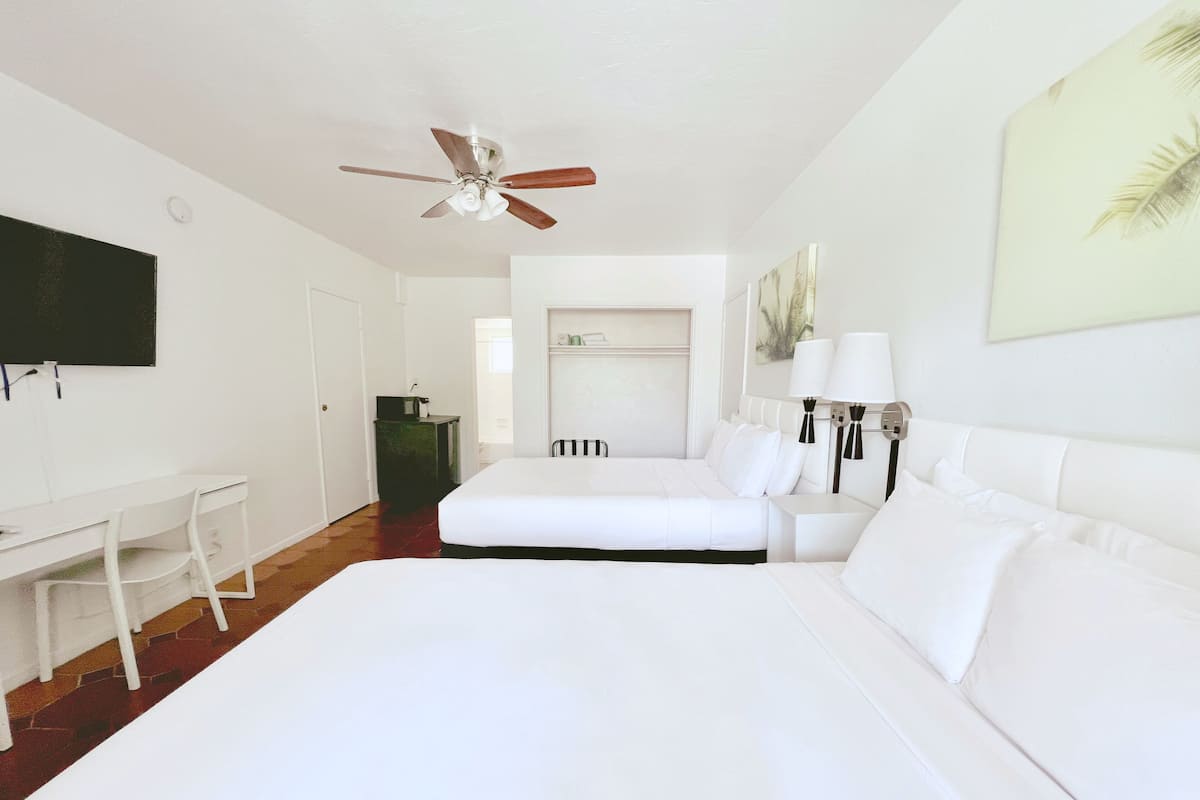 A hotel room with a large bed, a desk, a chair, a ceiling fan, and a TV mounted on the wall.