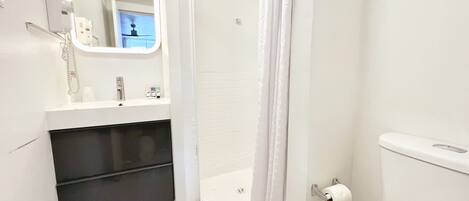 Une salle de bain avec des toilettes blanches, un lavabo avec un miroir, une douche avec un rideau et un porte-serviettes.