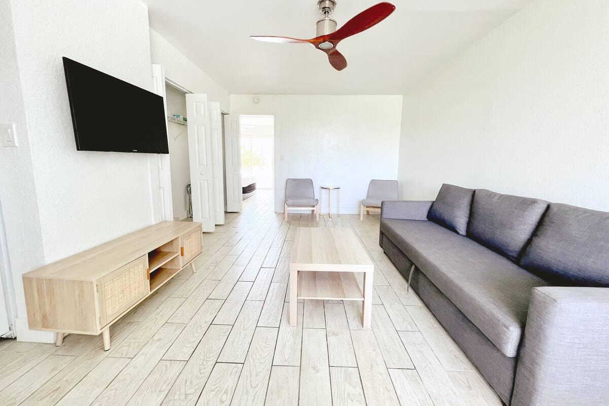 A modern living room with a grey sofa, wooden coffee table, and a flat-screen TV mounted on the wall.