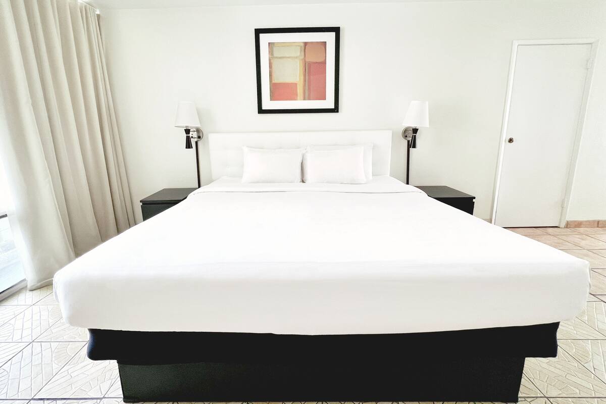 A hotel room with a large bed, two bedside tables, a framed picture on the wall, and a door.