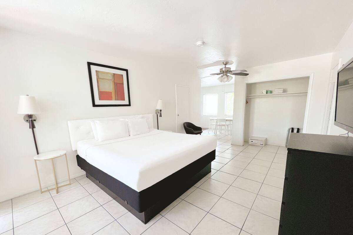 A modern hotel room with a large bed, a ceiling fan, a TV, and a desk.