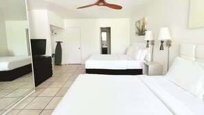 A hotel room with a large bed, a television, a wardrobe, a mirror, a ceiling fan, and a bathroom visible through an open door.