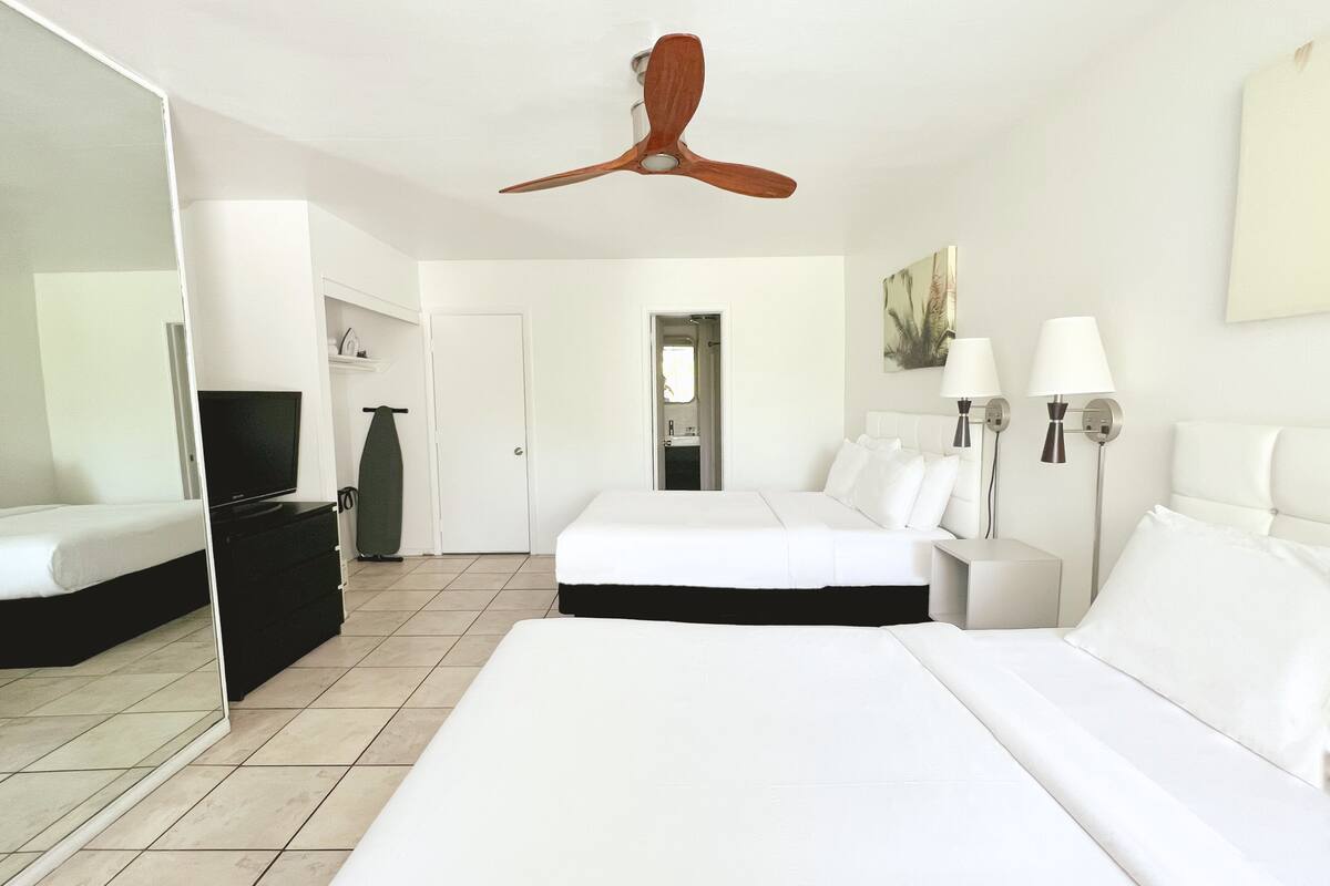 A hotel room with a large bed, a television, a wardrobe, a mirror, a ceiling fan, and a bathroom visible through an open door.