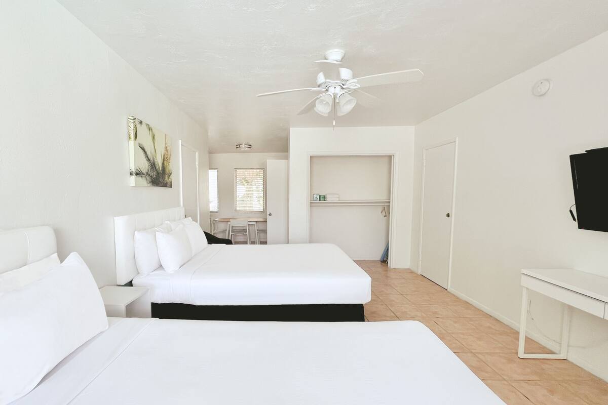 A hotel room with two beds, a desk, a chair, a TV, and a ceiling fan.