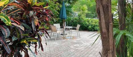A patio area with hexagonal paving, a table with chairs, and a green umbrella.