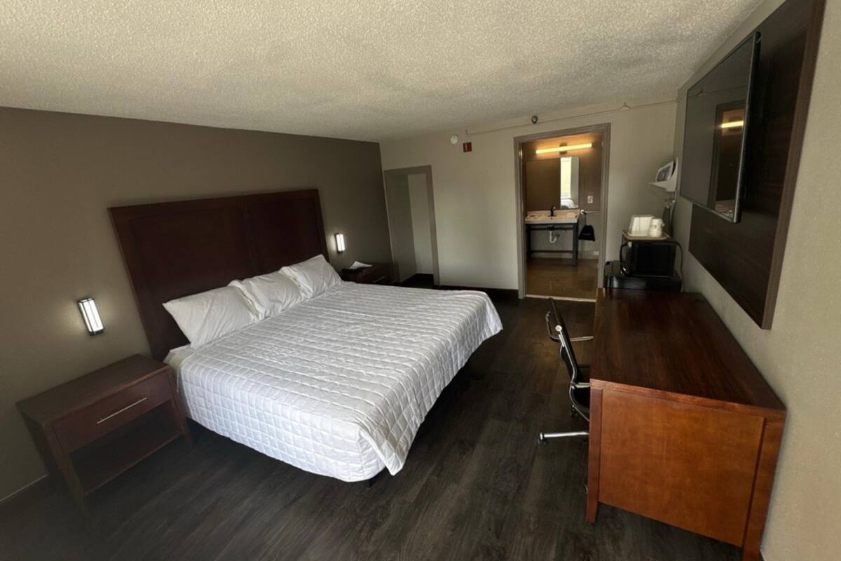 A hotel room with a bed, bedside table, desk, chair, and a mirror.