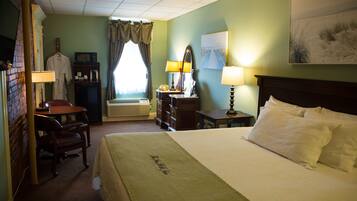 A hotel room with a bed, a desk with a chair, a dresser, a mirror, and a window with curtains.