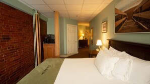 A hotel room with a bed, a desk, a lamp, a television, and a brick wall. - Inn at St John Portland In-Town (Portland)