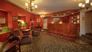 A hotel lobby with a reception desk, several armchairs, a patterned carpet, and a red wall with framed pictures. - Inn at St John Portland In-Town (Portland)
