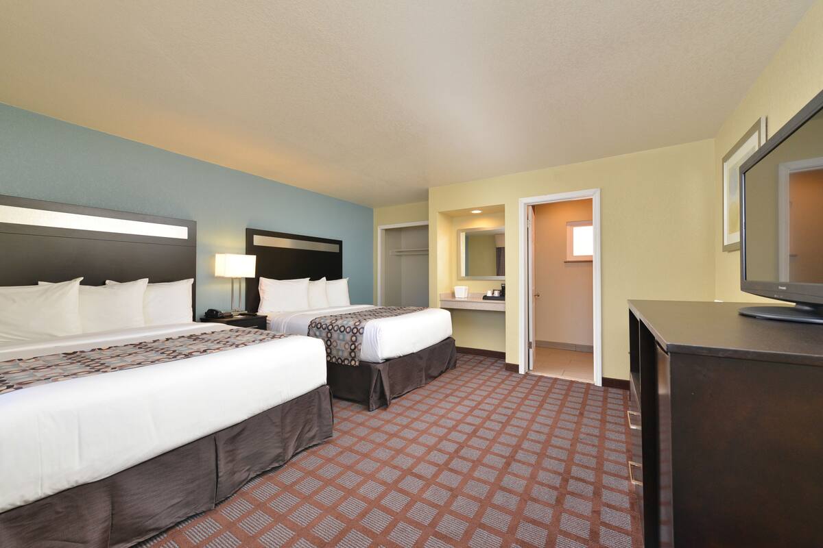 Ein Hotelzimmer mit zwei Betten, einem Schreibtisch, einem Fernseher und einem durchgegangenen Badezimmer.