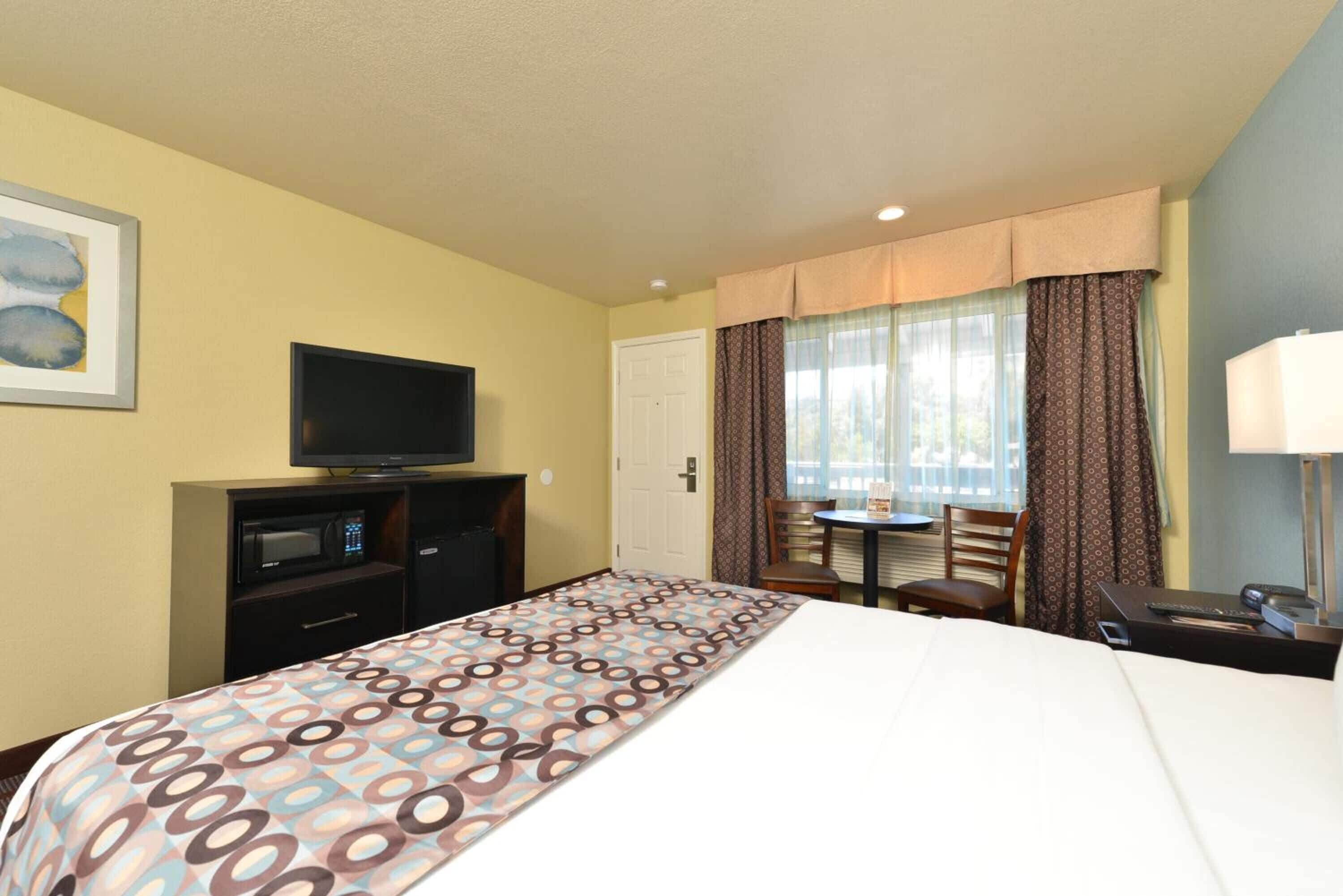 A hotel room with a bed, a television, a desk, and a window with curtains.