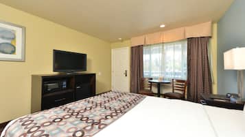 A hotel room with a bed, a television, a desk, and a window with curtains.