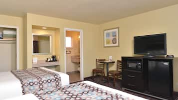 A hotel room with two beds, a desk with a chair, a television, a refrigerator, and a bathroom visible through an open door.