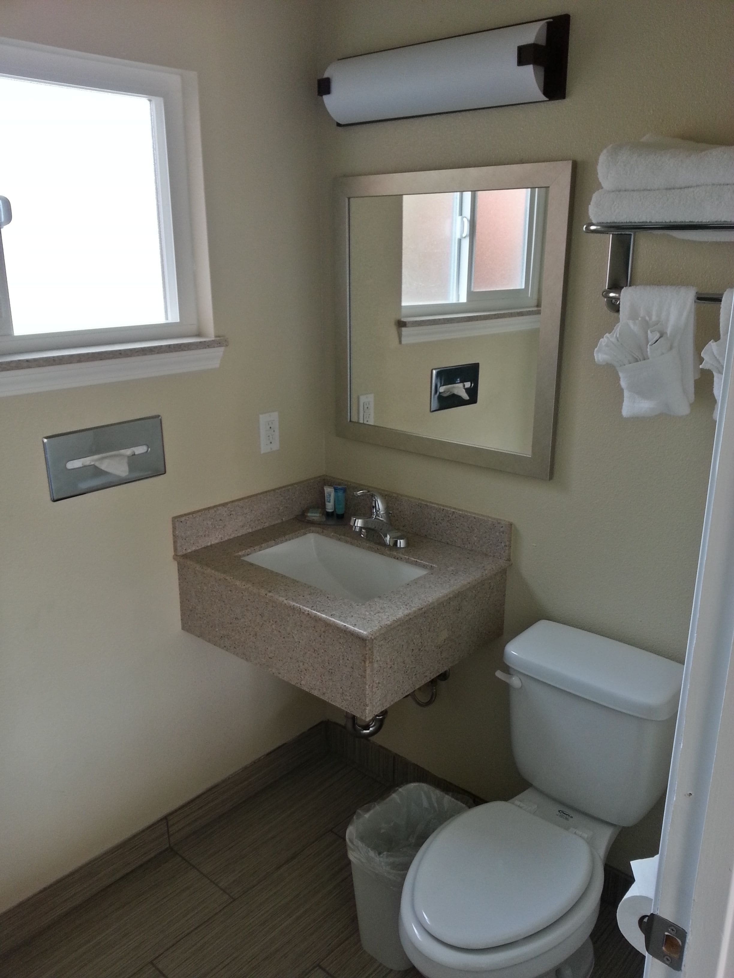 A bathroom with a sink, mirror, toilet, and a window.