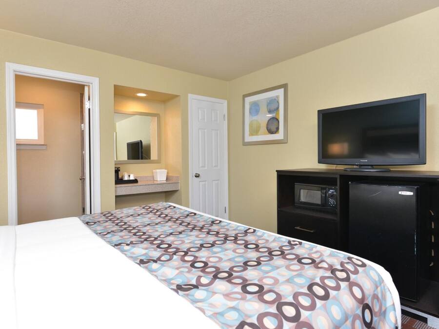 A hotel room with a bed, a television, a small refrigerator, a mirror, and a door leading to another room.