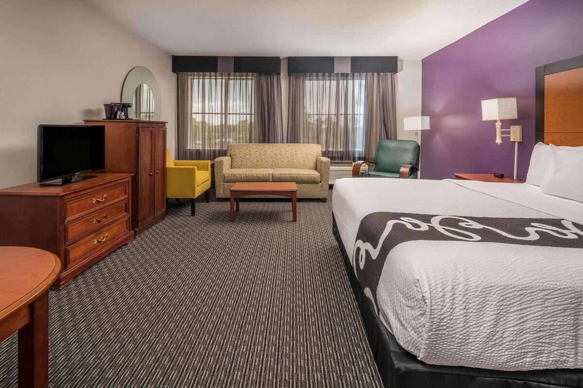 A hotel room with a bed, a television, a desk, a chair, a sofa, and a window with curtains.