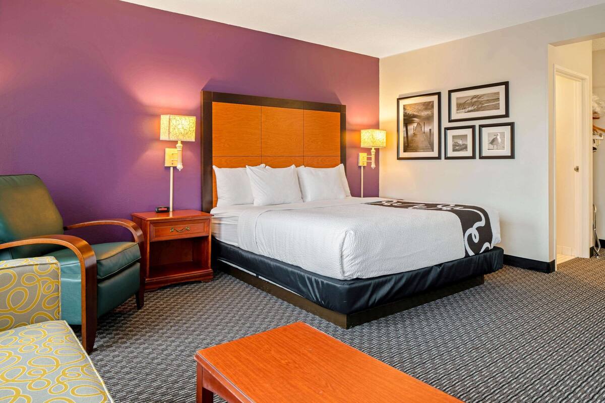 A hotel room with a large bed, a nightstand, a chair, and a small table.