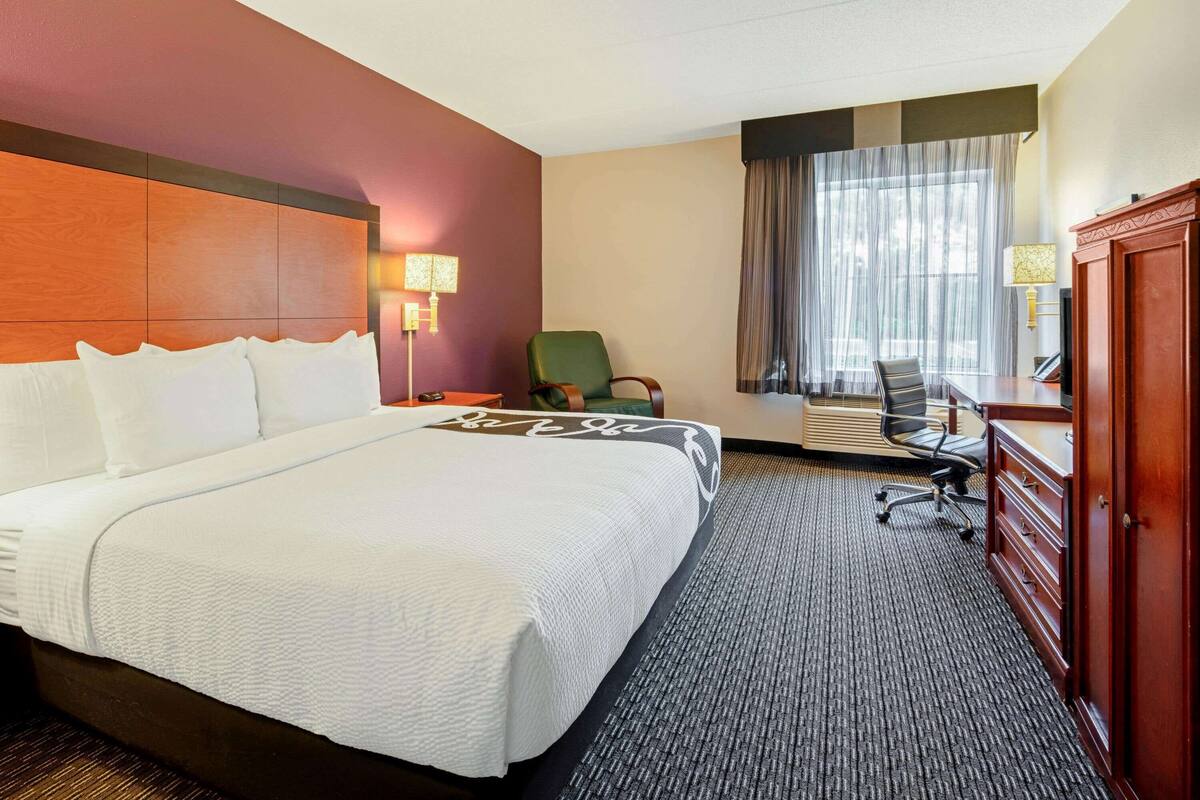 A hotel room with a large bed, a desk, a chair, and a wardrobe.