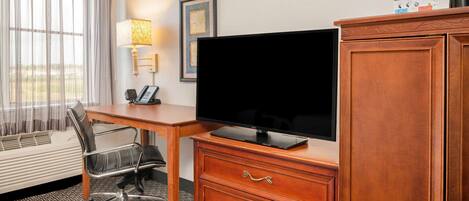 A hotel room with a desk, chair, television, and a cabinet.