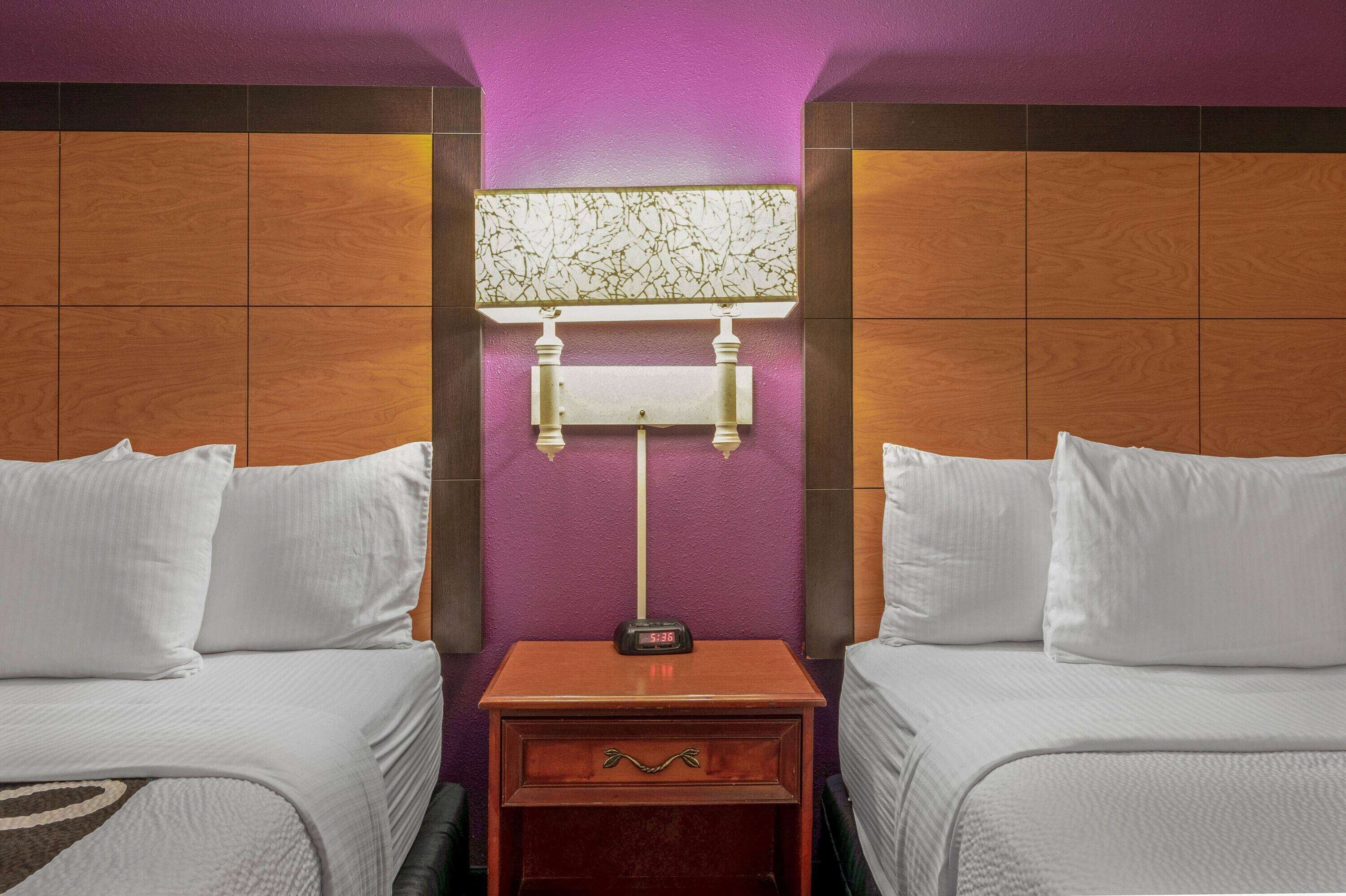 Una camera d'albergo con due letti, un comodino con una sveglia e una lampada a parete.