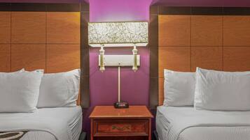 A hotel room with two beds, a nightstand with a clock, and a wall-mounted lamp.